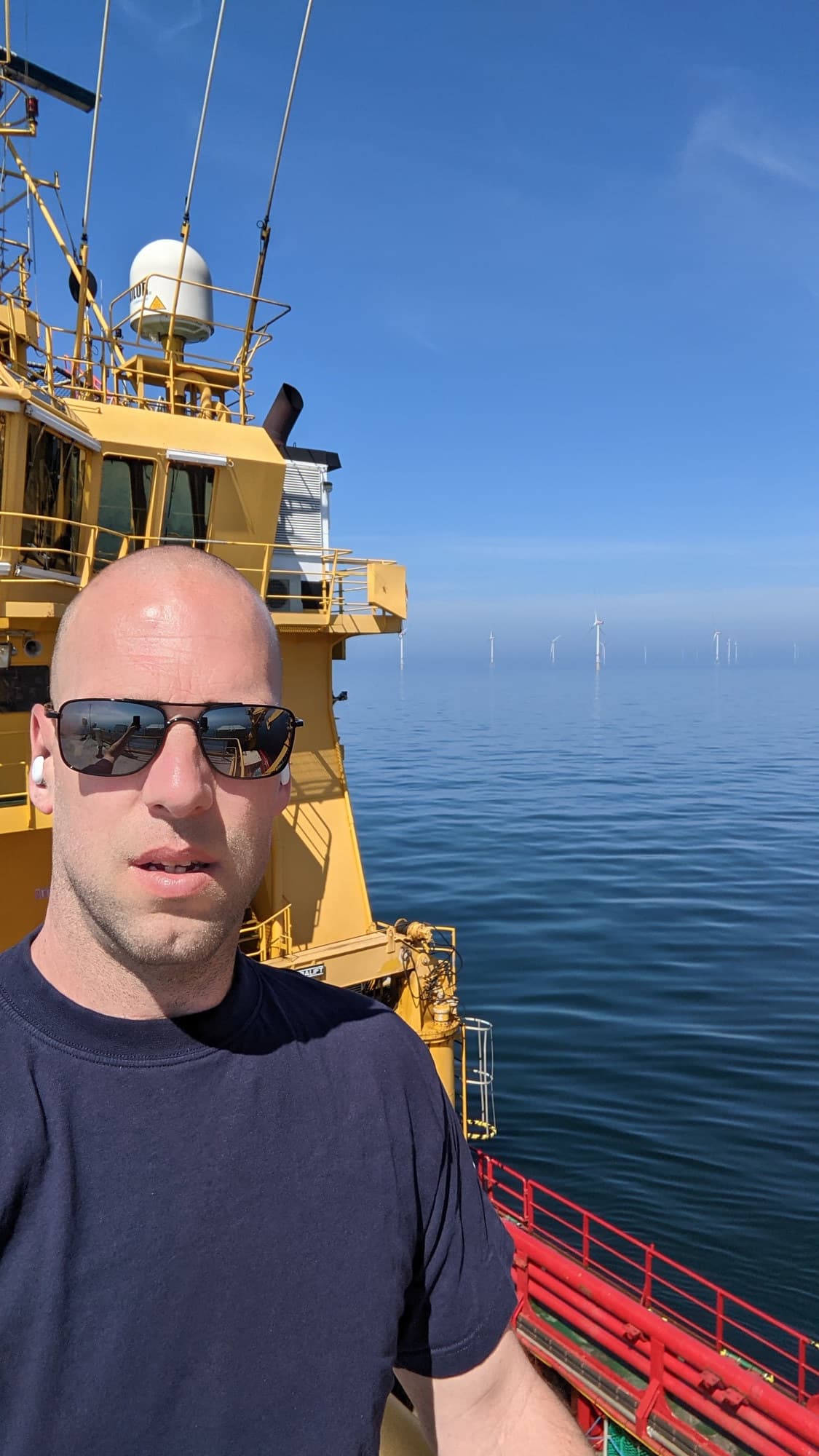 The instructor on the deck of a yellow workboat, with an offshore wind farm on the horizon.